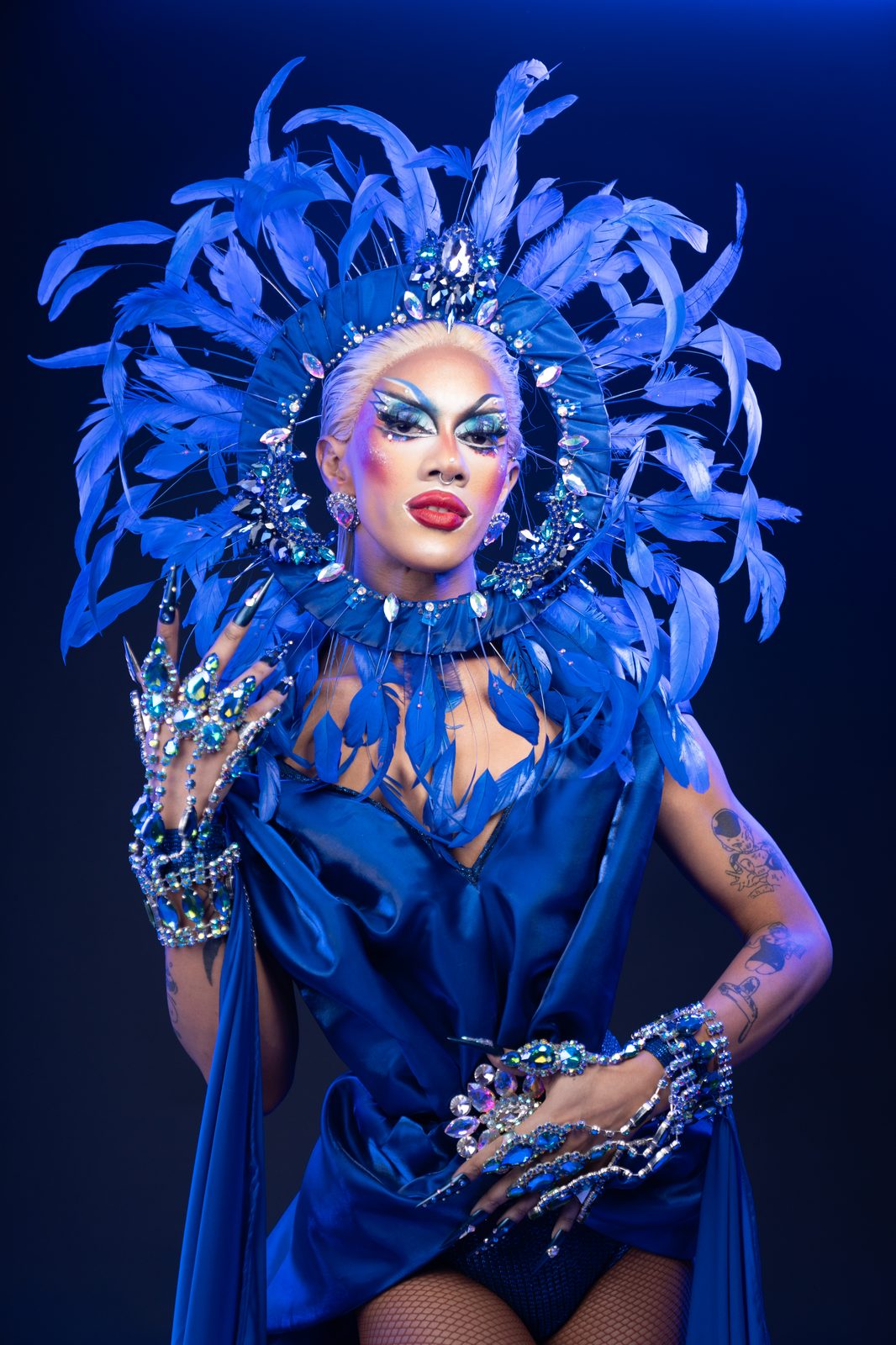 Ina Propriette in an elaborate blue feathered headdress and jewelled gauntlets, from The Blueprint