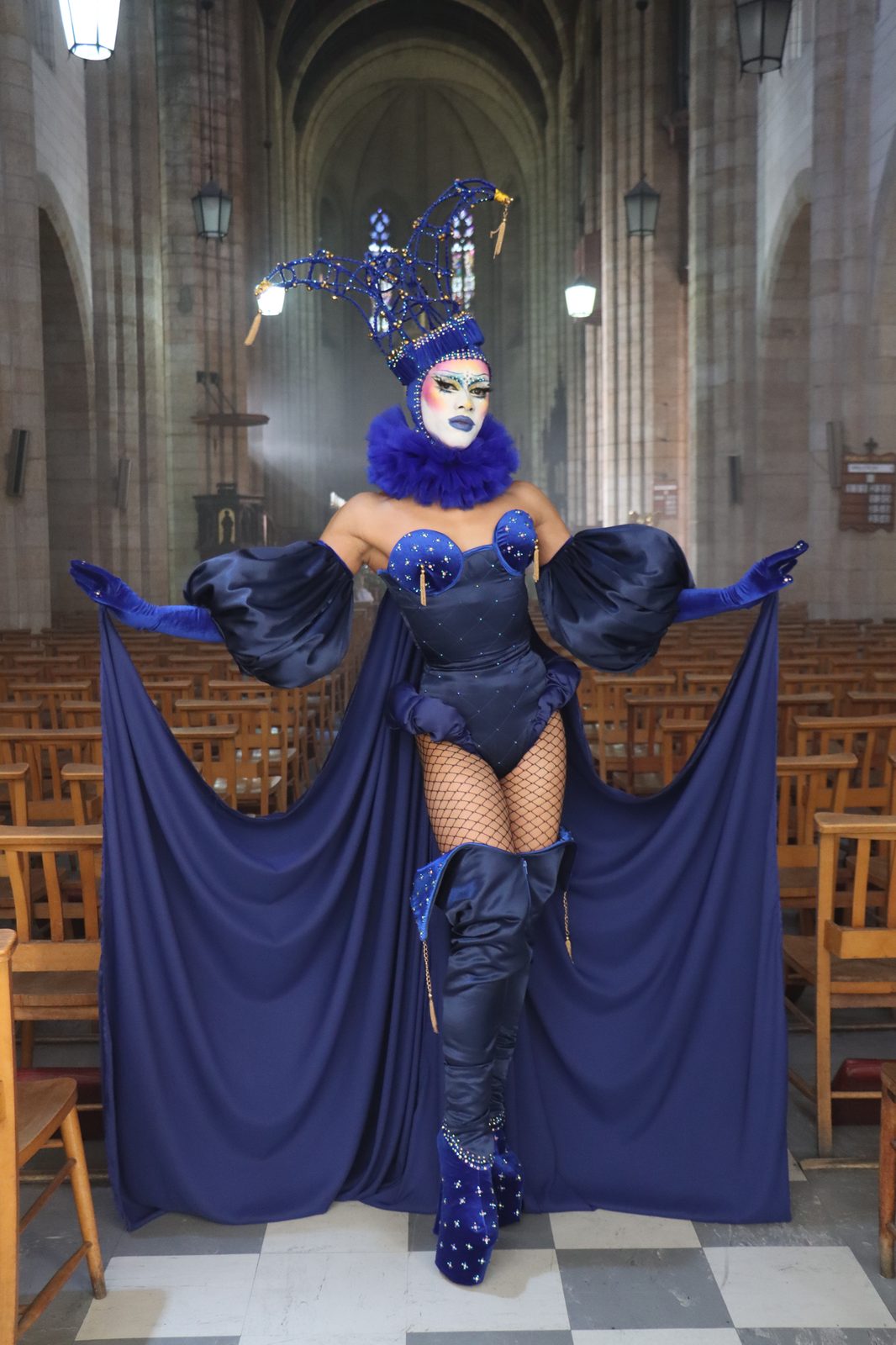 Ina Propriette in a navy blue caped costume and horned headdress inside a cathedral