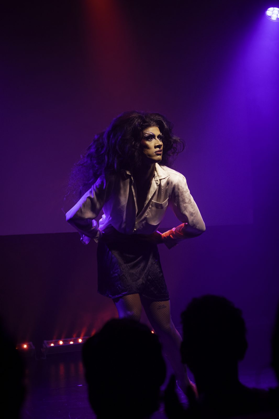 Ina Propriette performing on stage under purple lighting in a white shirt and tie