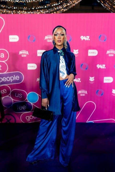 Ina Propriette in a blue satin suit on a red carpet at a media event