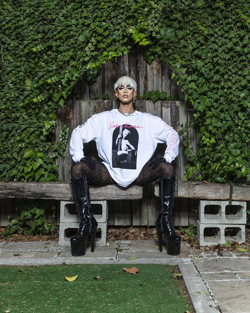 Ina Propriette in an oversized white graphic sweatshirt, seated on a bench