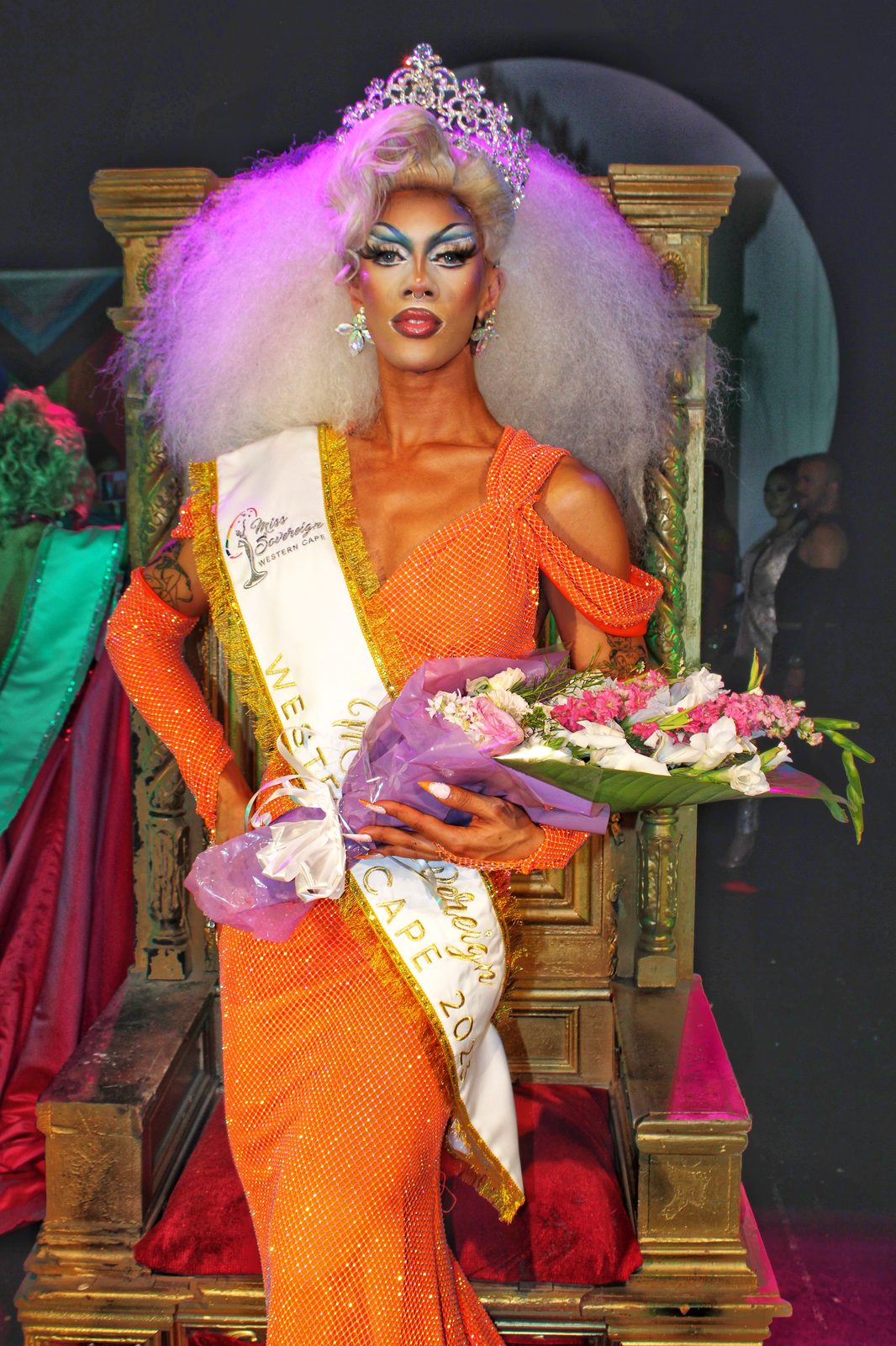 Ina Propriette crowned Miss Sovereign Western Cape 2023, wearing an orange gown, crown and sash, seated on a gold throne