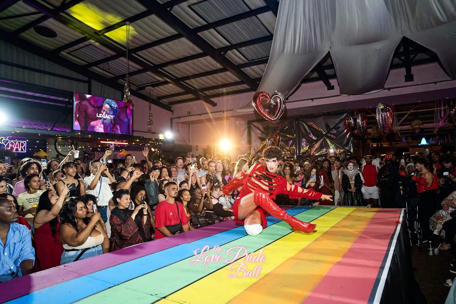 Ina Propriette performing a dip on a rainbow-painted runway in a red outfit at The Love Pride Ball